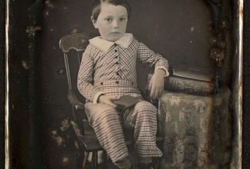 Damaged photograph of young boy sitting in chair