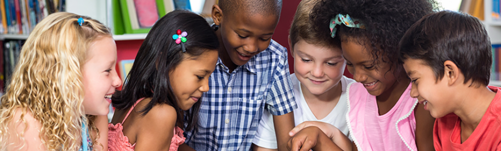 A group of children in a library gather around a tablet computer