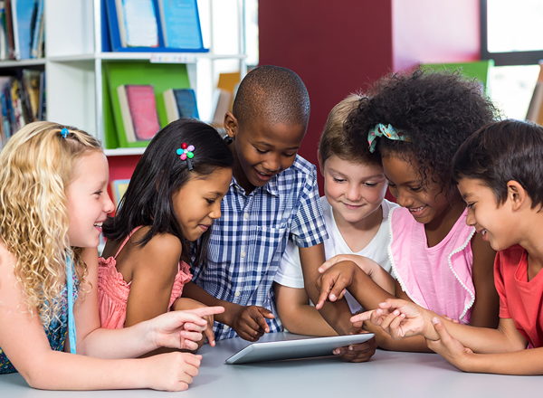 A group of children in a library gather around a tablet computer