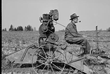 Man in a field operating an early tractor and smoking a pipe